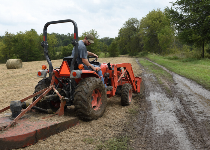2WD vs 4WD Farm Tractor Choice: Loader Work, Wet Fields, Slopes, and Ownership Tradeoffs 2 Compact tractor stopped beside dry hay field and muddy access lane