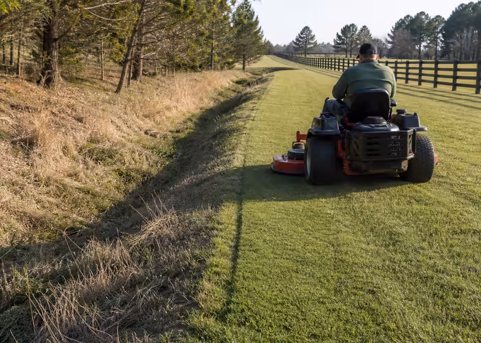 Zero-turn mower leaving a clean edge with a wide exit line beside a shallow ditch